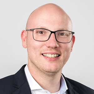 Porträt eines smiling Mannes mit Brille, der in einem formellen Outfit abgebildet ist, geeignet für geschäftliche Anwendungen.